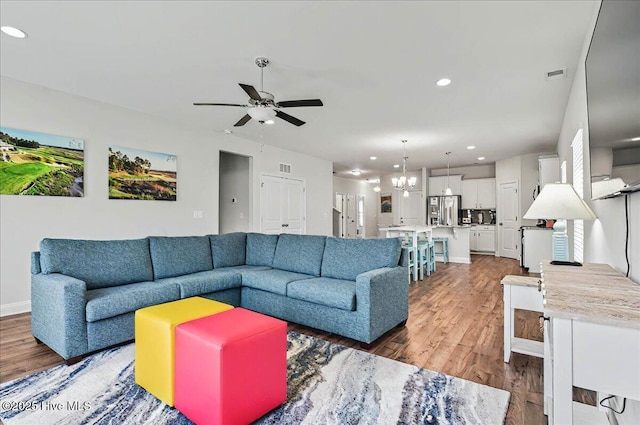 living room with wood finished floors, ceiling fan with notable chandelier, visible vents, baseboards, and recessed lighting