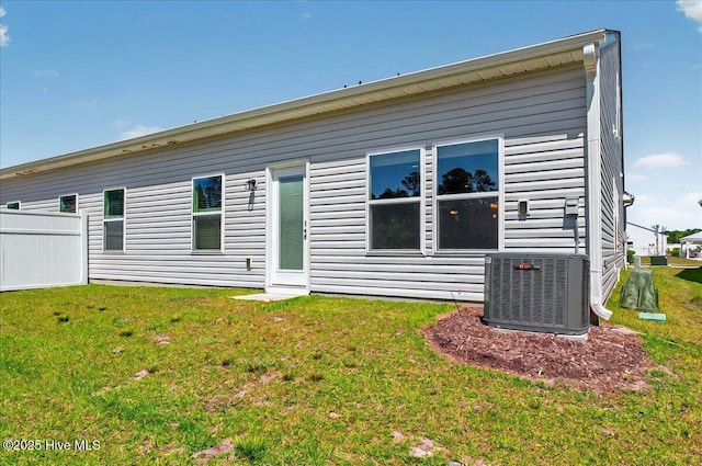 rear view of property featuring a lawn, central air condition unit, and fence