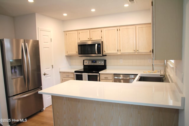 kitchen with backsplash, light countertops, a sink, a peninsula, and stainless steel appliances