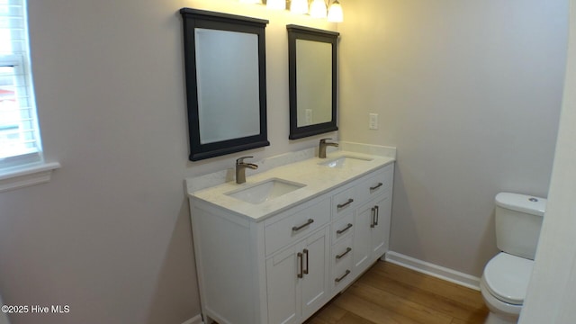 bathroom featuring double vanity, a sink, wood finished floors, and toilet