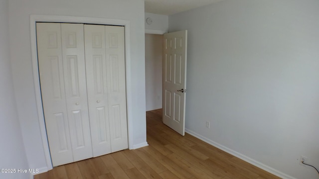 unfurnished bedroom featuring baseboards, light wood-style flooring, and a closet