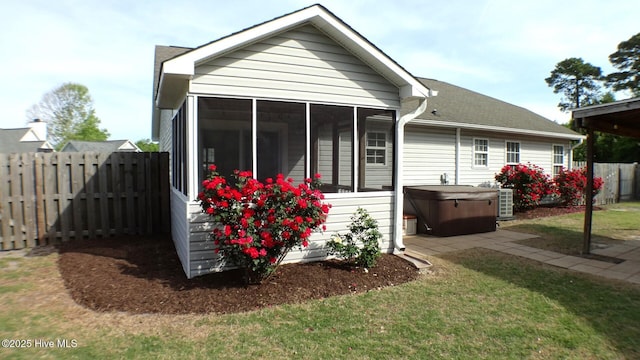 back of property with a hot tub, a sunroom, a fenced backyard, cooling unit, and a lawn