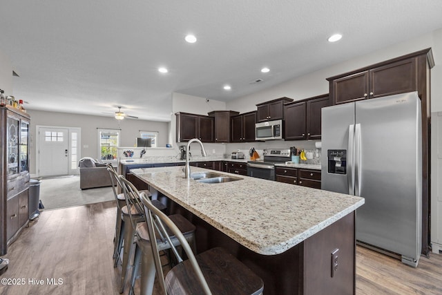 kitchen featuring dark brown cabinets, a breakfast bar, a sink, light wood-style flooring, and appliances with stainless steel finishes
