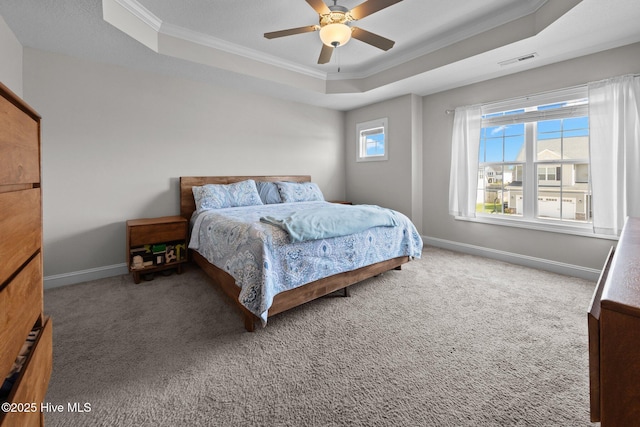 carpeted bedroom with a ceiling fan, visible vents, a raised ceiling, baseboards, and ornamental molding