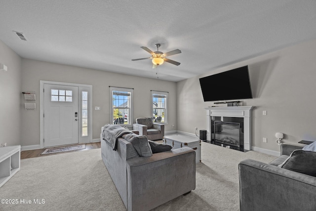 carpeted living area with ceiling fan, visible vents, plenty of natural light, and a fireplace with flush hearth