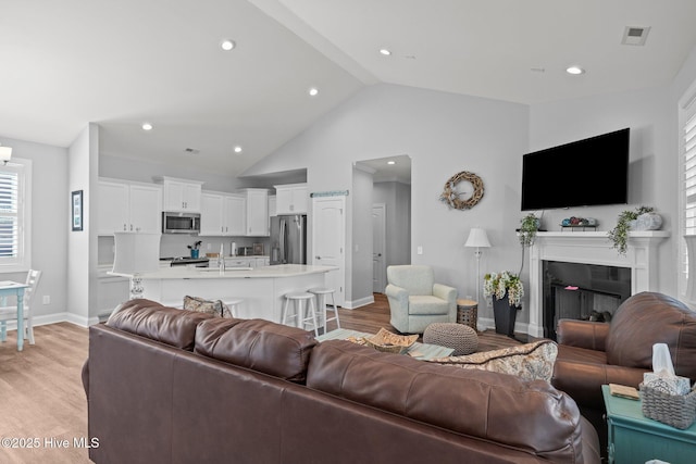 living area featuring visible vents, light wood finished floors, baseboards, and lofted ceiling