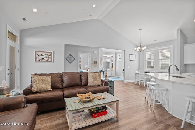 living area featuring visible vents, wood finished floors, a chandelier, and vaulted ceiling