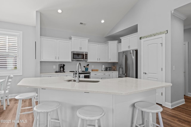 kitchen featuring a kitchen breakfast bar, white cabinetry, a sink, stainless steel appliances, and baseboards