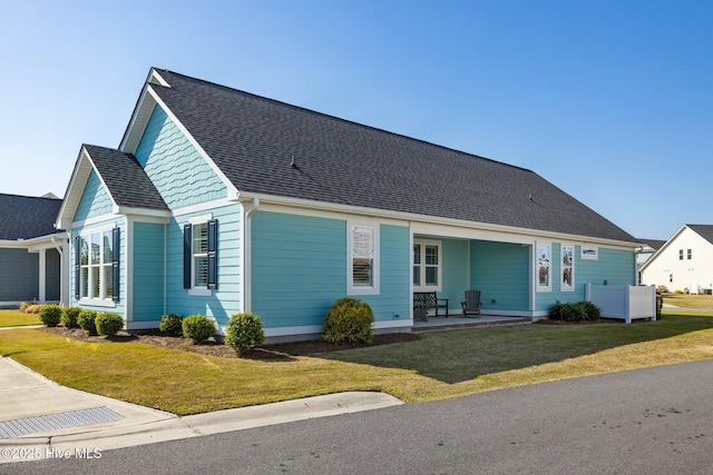 view of front of home featuring a patio, a shingled roof, and a front lawn