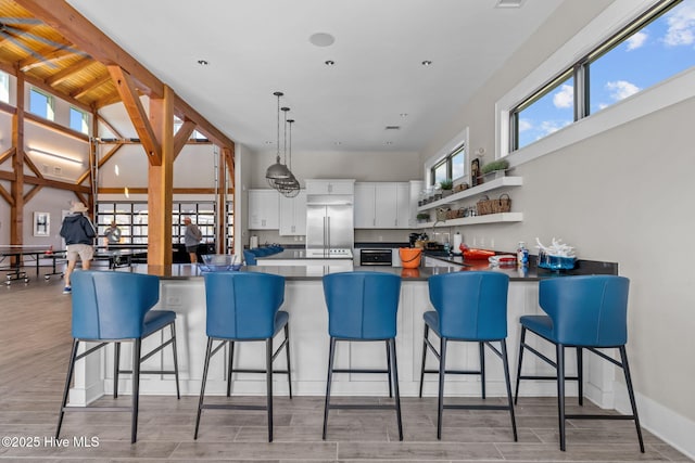 kitchen with a peninsula, stainless steel built in refrigerator, dark countertops, and white cabinetry