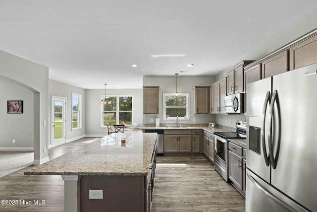 kitchen with a kitchen island, appliances with stainless steel finishes, wood finished floors, a sink, and light stone counters