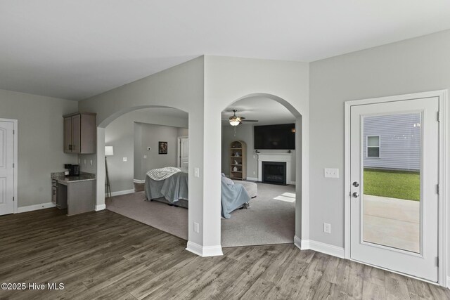 unfurnished living room featuring baseboards, a ceiling fan, a fireplace, and dark wood finished floors