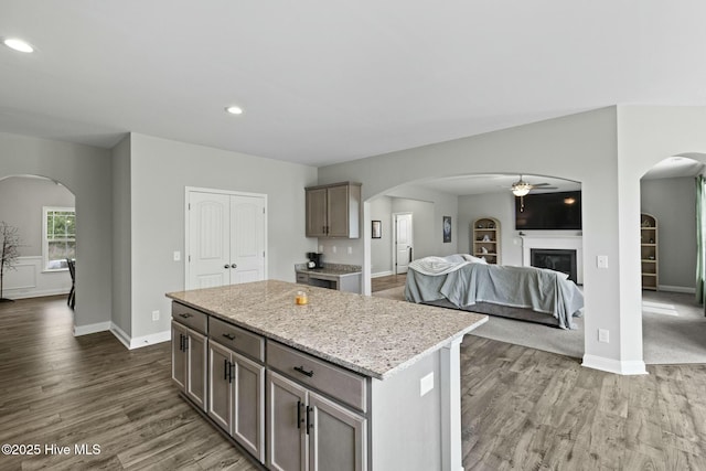 kitchen with open floor plan, a center island, a ceiling fan, dark wood finished floors, and arched walkways