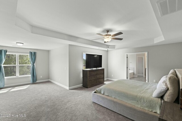 carpeted bedroom with connected bathroom, a tray ceiling, a ceiling fan, visible vents, and baseboards