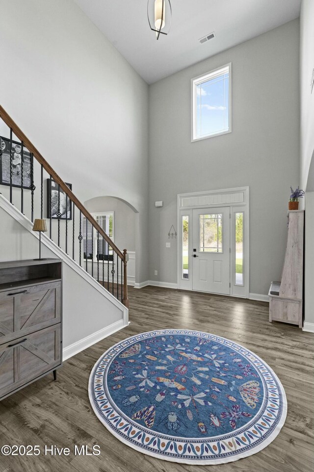 entrance foyer featuring stairway, a towering ceiling, baseboards, and wood finished floors