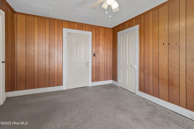 unfurnished bedroom featuring wooden walls, a ceiling fan, and carpet floors