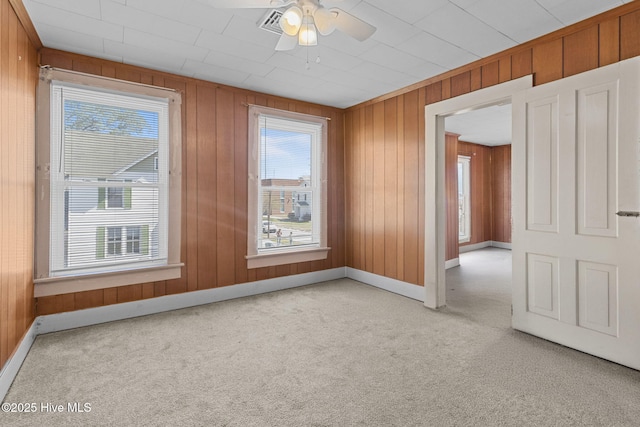 carpeted spare room featuring wood walls, baseboards, a ceiling fan, and plenty of natural light