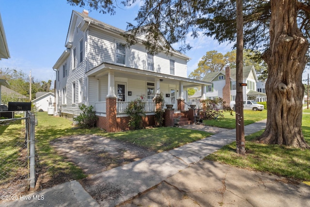 view of front facade with a porch, a chimney, a front yard, and fence