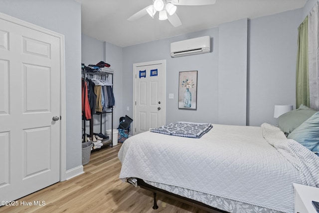 bedroom featuring baseboards, a closet, a wall unit AC, ceiling fan, and light wood finished floors