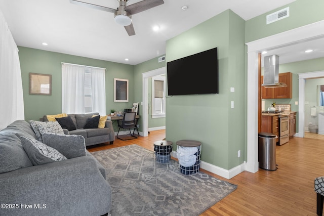 living room featuring light wood finished floors, visible vents, baseboards, and a ceiling fan