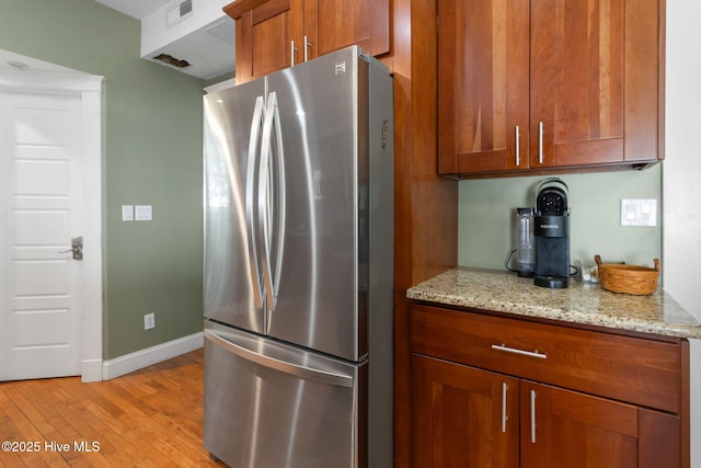 kitchen featuring visible vents, baseboards, freestanding refrigerator, light wood-type flooring, and brown cabinets