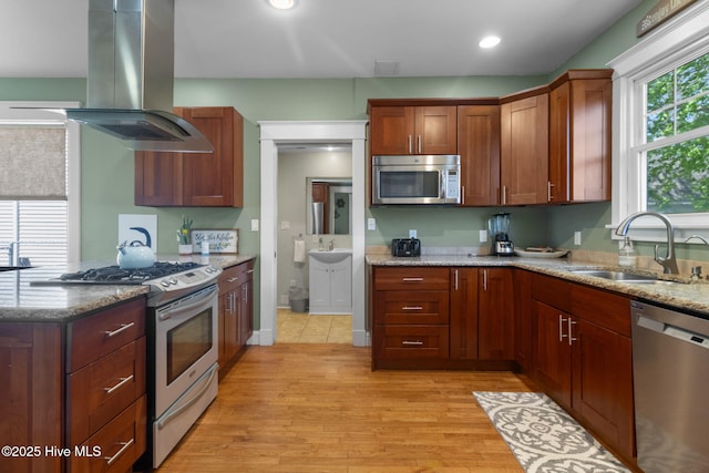 kitchen featuring stainless steel appliances, a sink, island exhaust hood, and light stone counters