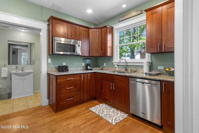 kitchen featuring light wood-style floors, appliances with stainless steel finishes, a sink, and light stone countertops