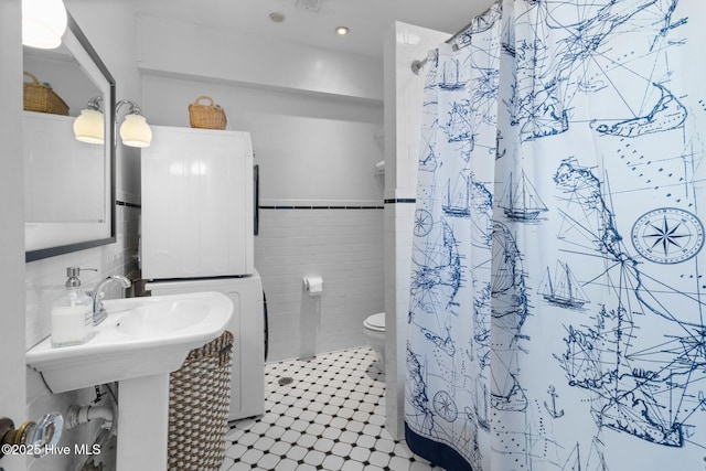 full bath with stacked washing maching and dryer, curtained shower, tile walls, and toilet