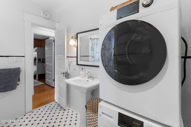 bathroom with stacked washer / dryer, tile patterned floors, wainscoting, and tile walls
