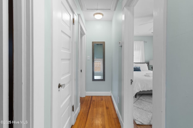 corridor with light wood-style flooring, baseboards, and attic access