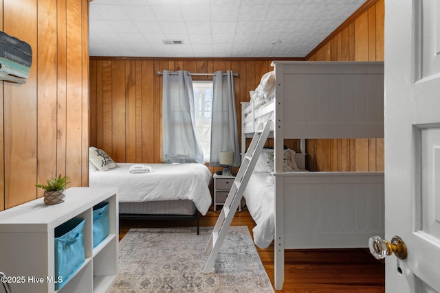 bedroom featuring wood finished floors, wood walls, and visible vents