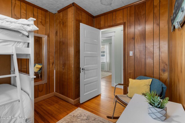 bedroom with light wood-style floors, crown molding, wooden walls, and baseboards