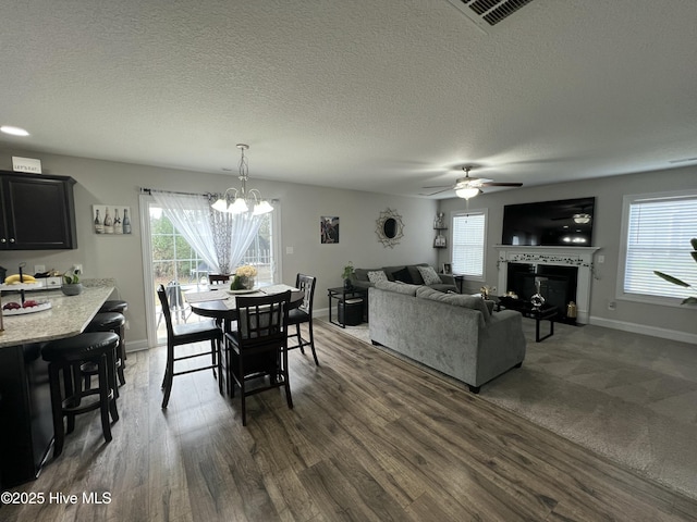dining space with a fireplace, dark wood-style floors, a textured ceiling, visible vents, and ceiling fan with notable chandelier