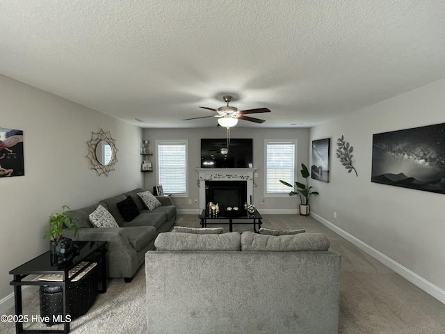 carpeted living area with a wealth of natural light, a fireplace, baseboards, and a ceiling fan