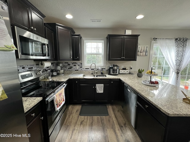kitchen with a peninsula, visible vents, appliances with stainless steel finishes, a sink, and dark cabinetry