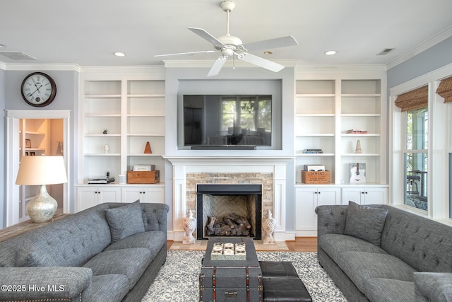living room featuring ceiling fan, visible vents, a fireplace, light wood finished floors, and ornamental molding