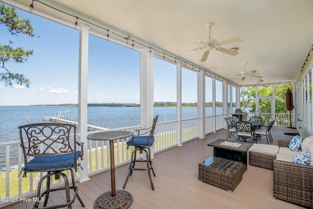 sunroom / solarium featuring a water view, ceiling fan, a wall of windows, and wood finished floors