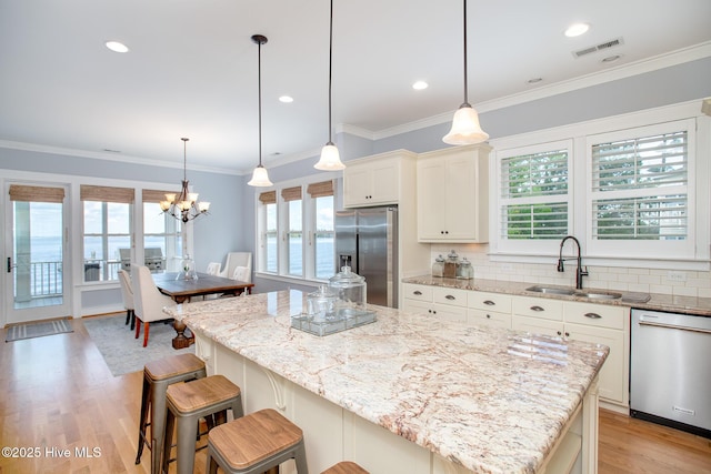 kitchen with a notable chandelier, appliances with stainless steel finishes, a sink, light wood-style floors, and decorative backsplash