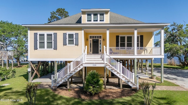 coastal inspired home featuring a front yard, roof with shingles, a porch, stairway, and a carport
