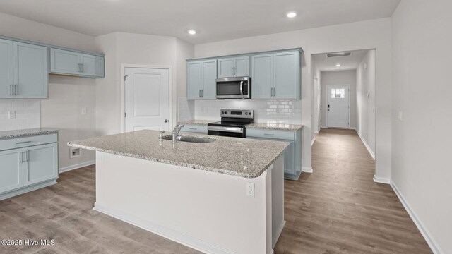 kitchen with light stone countertops, appliances with stainless steel finishes, wood finished floors, a sink, and baseboards