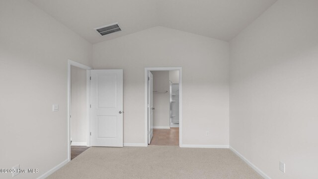 unfurnished bedroom with baseboards, carpet floors, a walk in closet, visible vents, and lofted ceiling