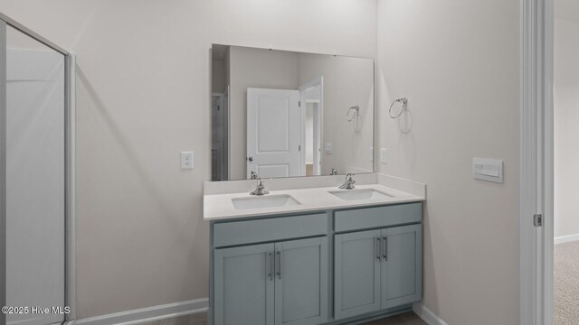 bathroom with a shower with shower door, double vanity, a sink, and baseboards