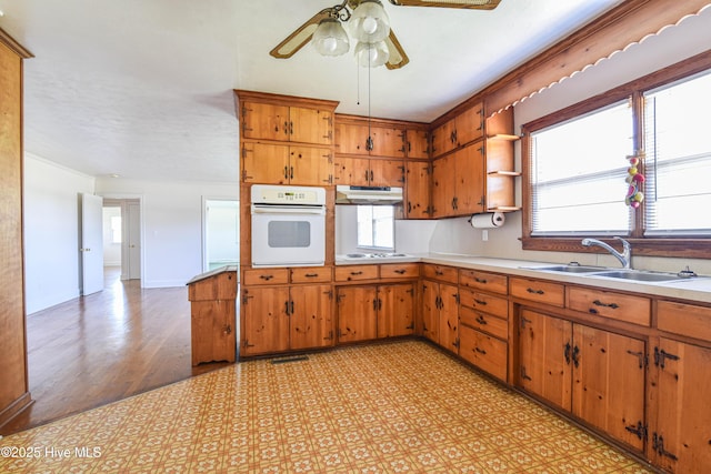 kitchen featuring white appliances, light countertops, a ceiling fan, under cabinet range hood, and a sink