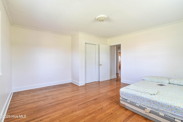 bedroom with ornamental molding, baseboards, a closet, and light wood-style floors