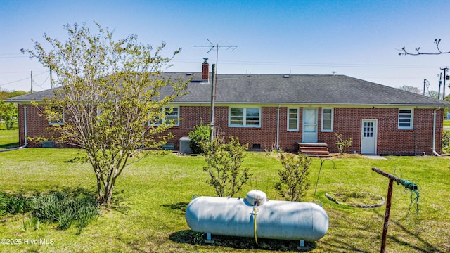 back of property featuring a yard, roof with shingles, brick siding, and a chimney