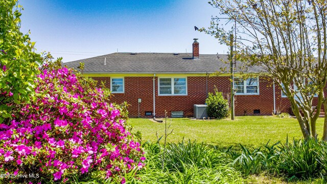 rear view of property with crawl space, a yard, brick siding, and a chimney