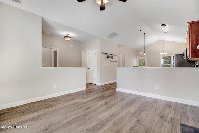 unfurnished living room with light wood-style flooring, ceiling fan with notable chandelier, vaulted ceiling, and visible vents