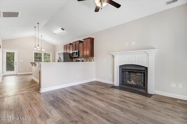 kitchen with visible vents, wood finished floors, ceiling fan with notable chandelier, a fireplace with flush hearth, and stainless steel appliances