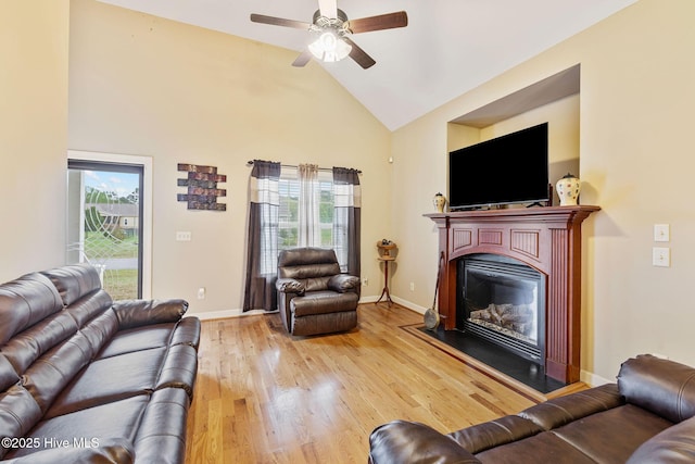 living room with baseboards, a ceiling fan, light wood finished floors, high vaulted ceiling, and a glass covered fireplace