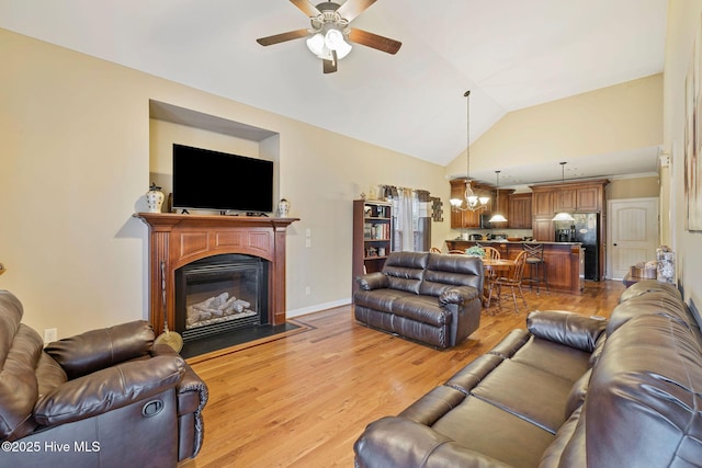 living room with light wood-style flooring, ceiling fan with notable chandelier, a glass covered fireplace, and vaulted ceiling